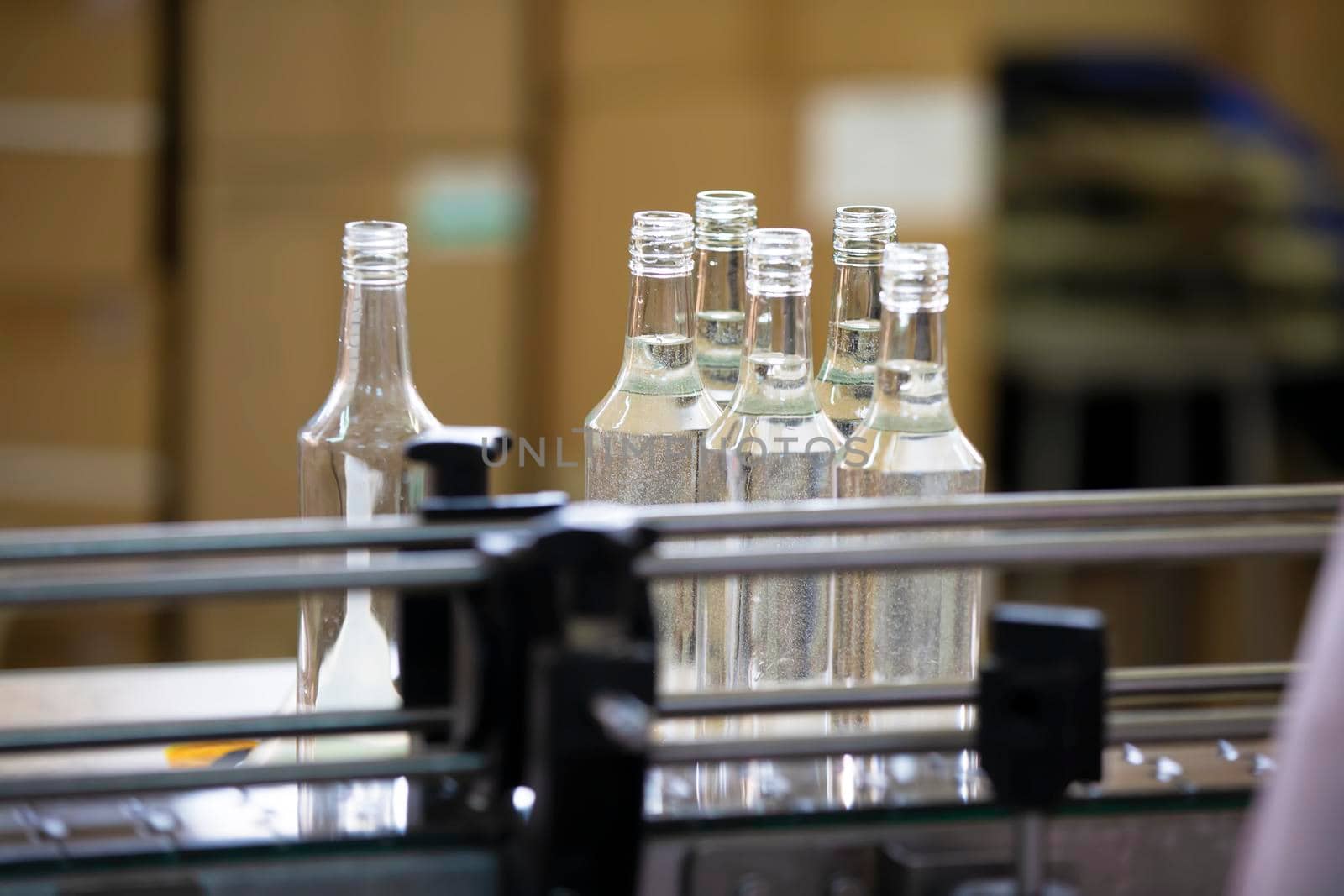 A row of glass bottles on a conveyor belt for the production of alcoholic beverages.