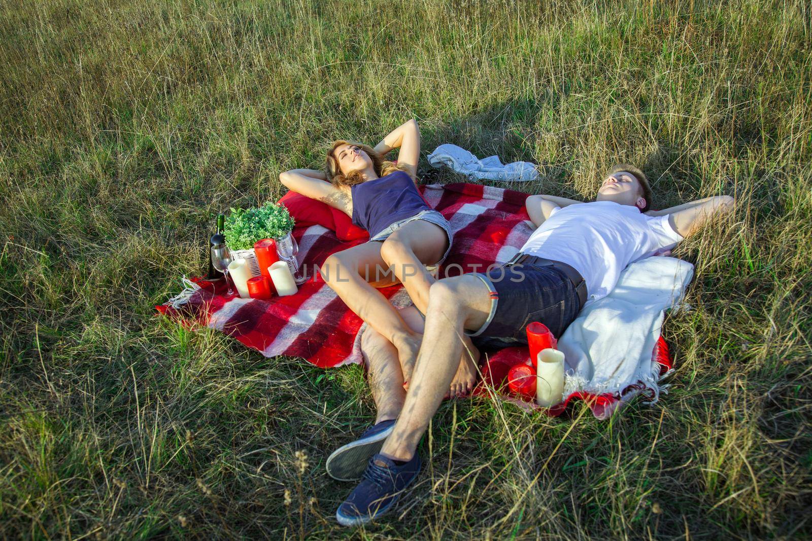 Young beautiful lovely couple lying down and have a rest on plaid in field on summer day and smiling.