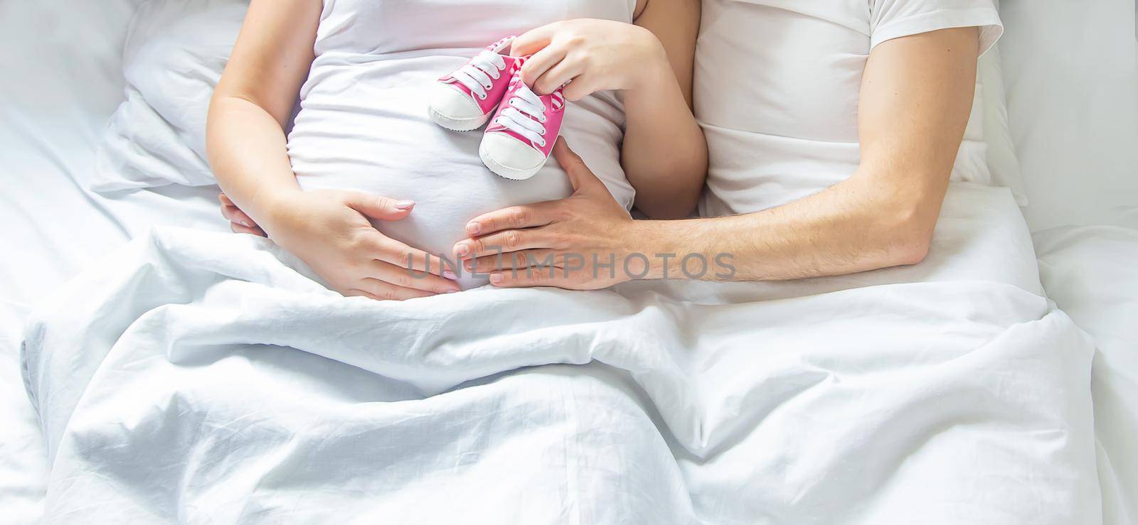 Pregnant woman and man hug belly and hold baby shoes. Selective focus. by yanadjana