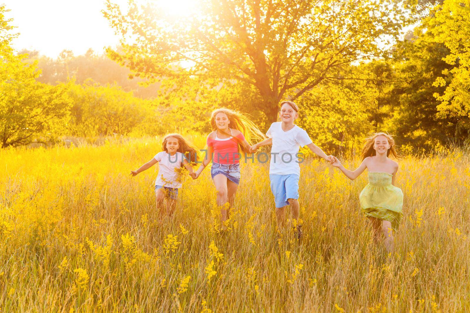 four happy beautiful children running playing moving together in the beautiful summer day. jumping and looking at camera with happiness and toothy smile.