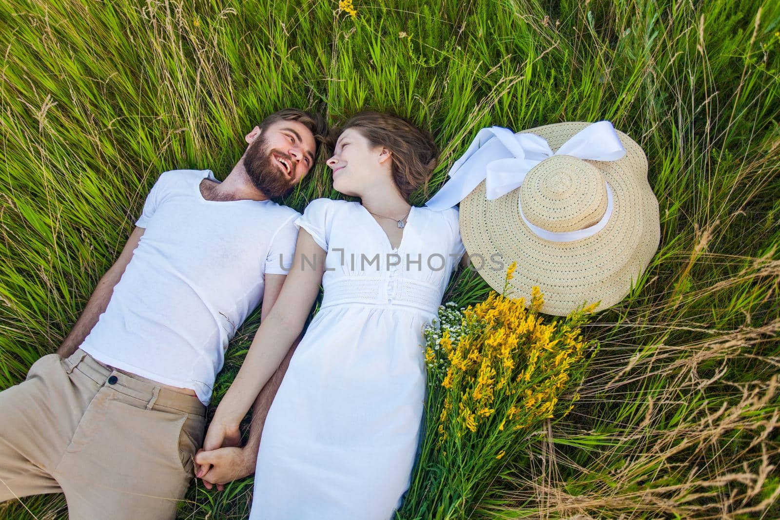 Happy young relaxed couple in love laying down on the grass overhead. outdoor summertime.