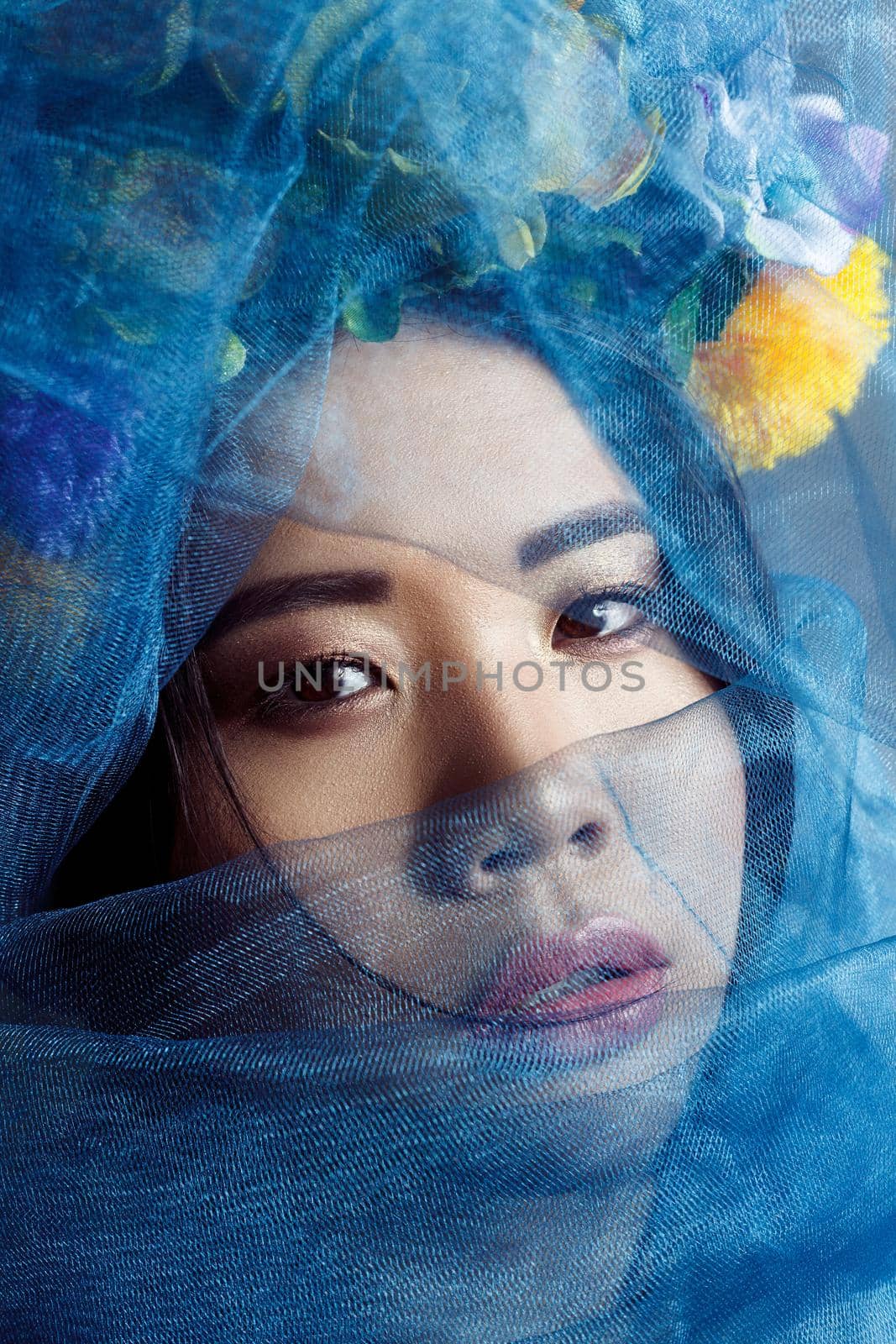 portrait of asian woman with floral hat and blue veil looking at camera on light grey background . indoor studio shot.