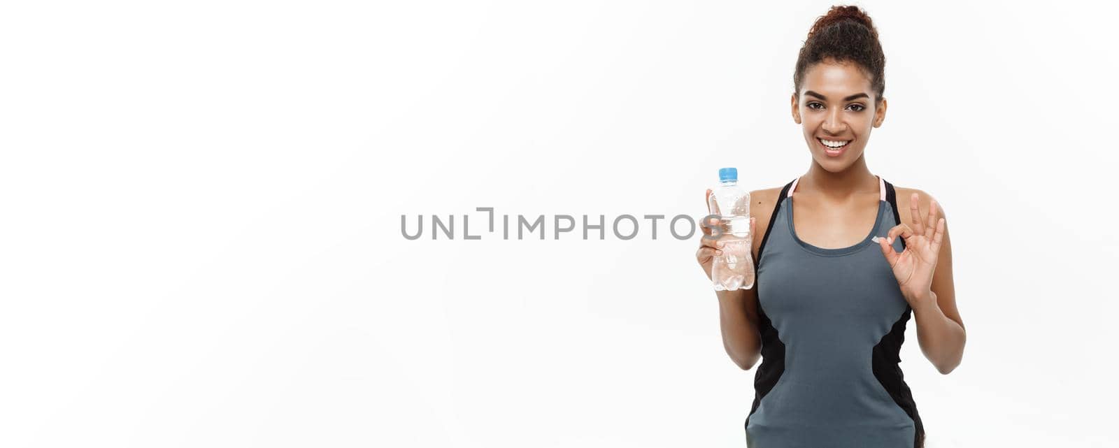 Healthy and Fitness concept - beautiful African American girl in sport clothes holding plastic water bottle after workout. Isolated on white studio background.