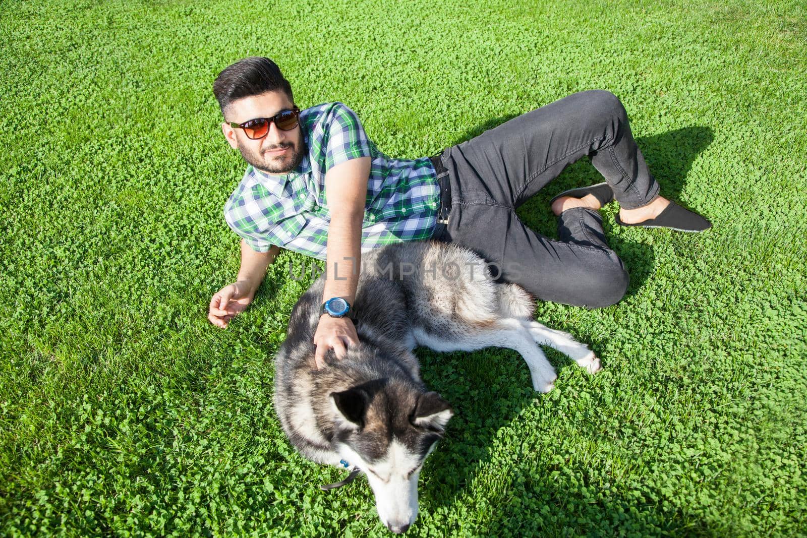 Young man sitting at green lawn and enjoying with his dog