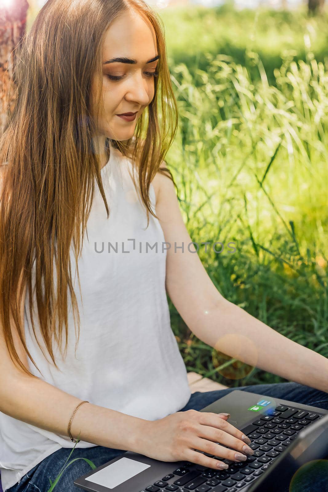On the banner, a young girl works with a laptop in the fresh air in the park, sitting on the lawn. The concept of remote work. Work as a freelancer. The girl takes courses on a laptop and smiles