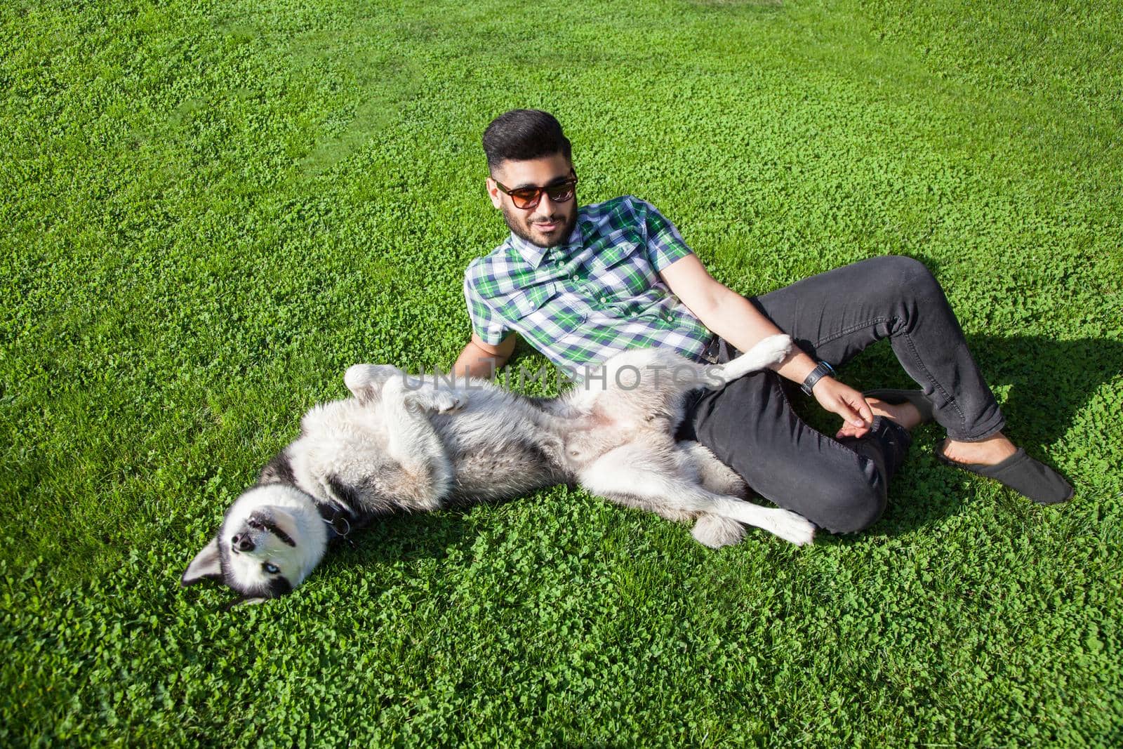 Young man sitting at green lawn and enjoying with his dog by Khosro1