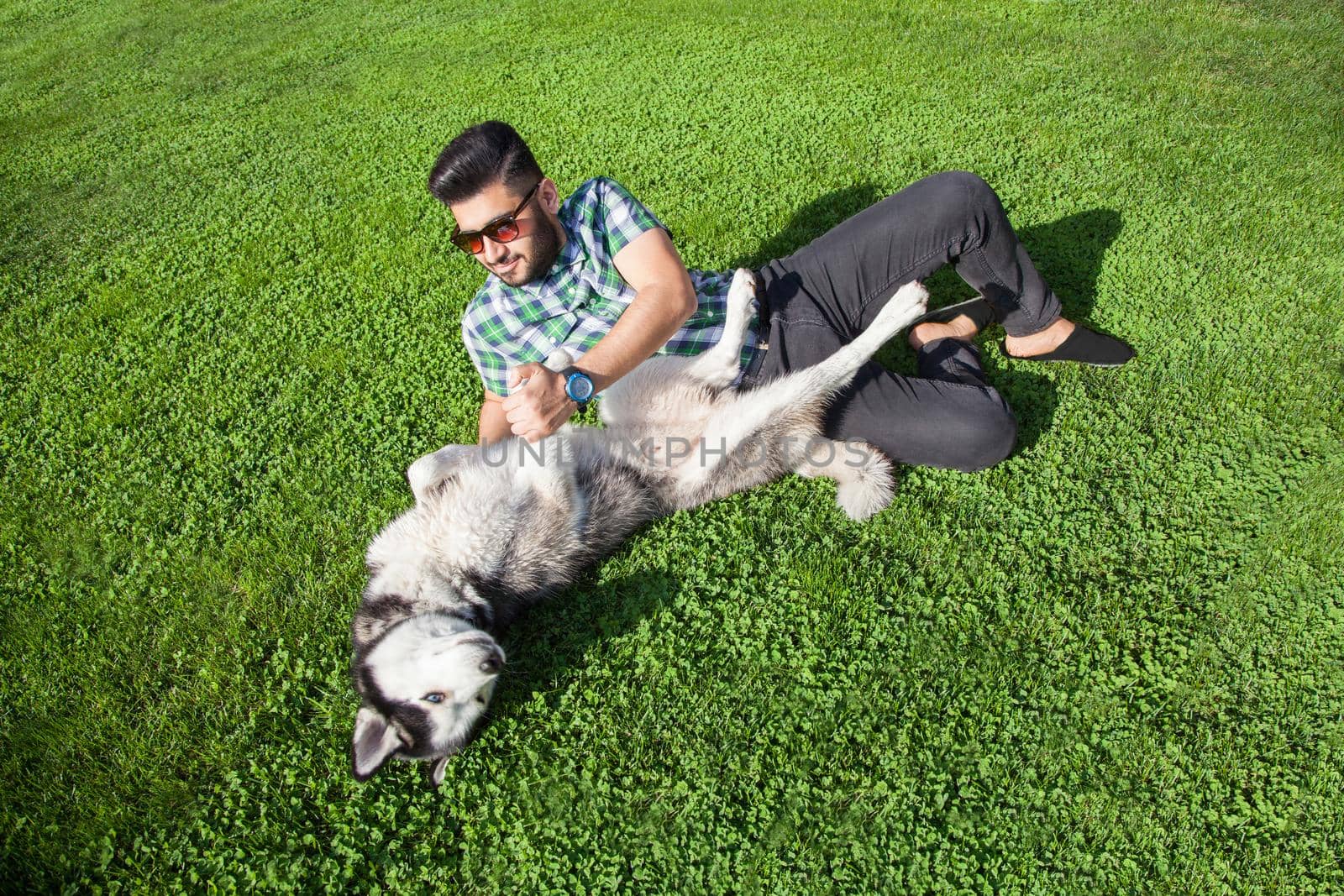 Young man sitting at green lawn and enjoying with his dog by Khosro1