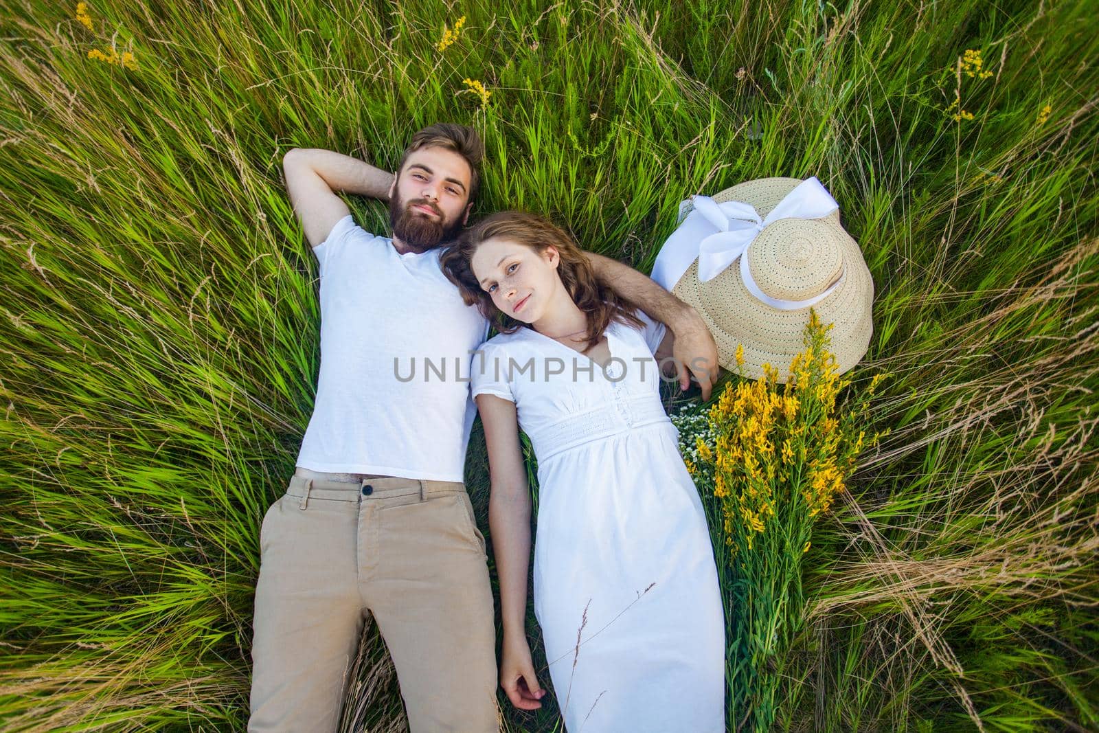 Happy young relaxed couple in love laying down on the grass overhead. outdoor summertime.