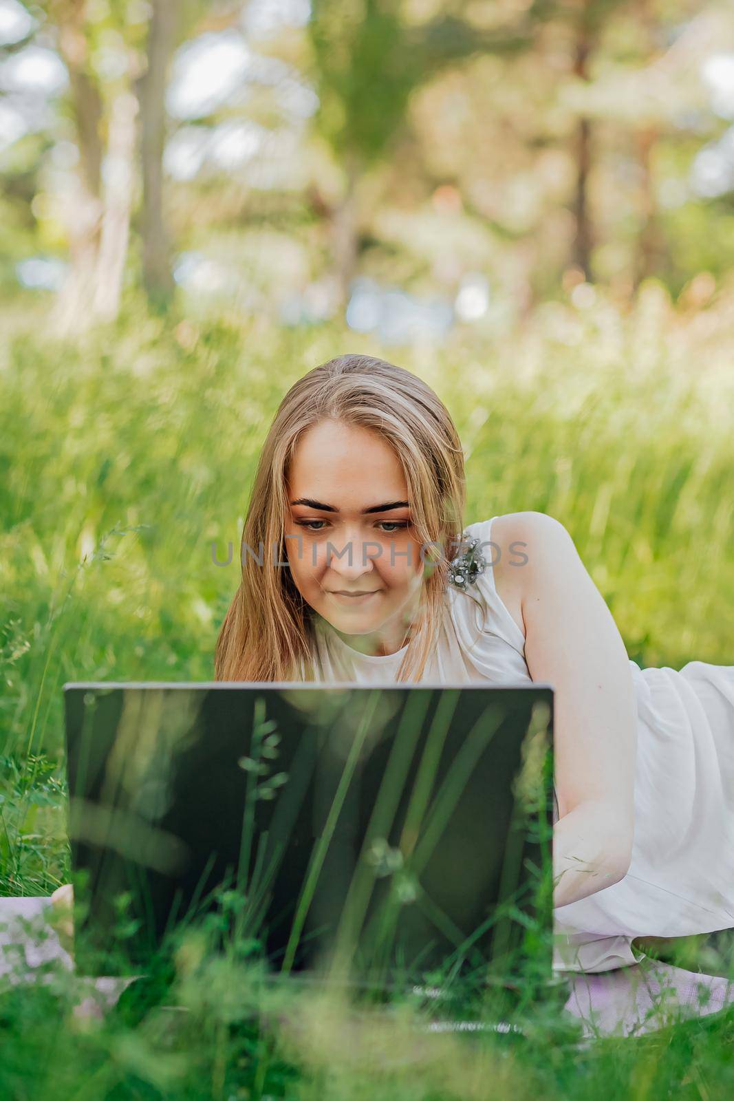 the girl sits on the grass and uses a laptop. Education, lifestyle, technology concept, outdoor learning concept by Anyatachka