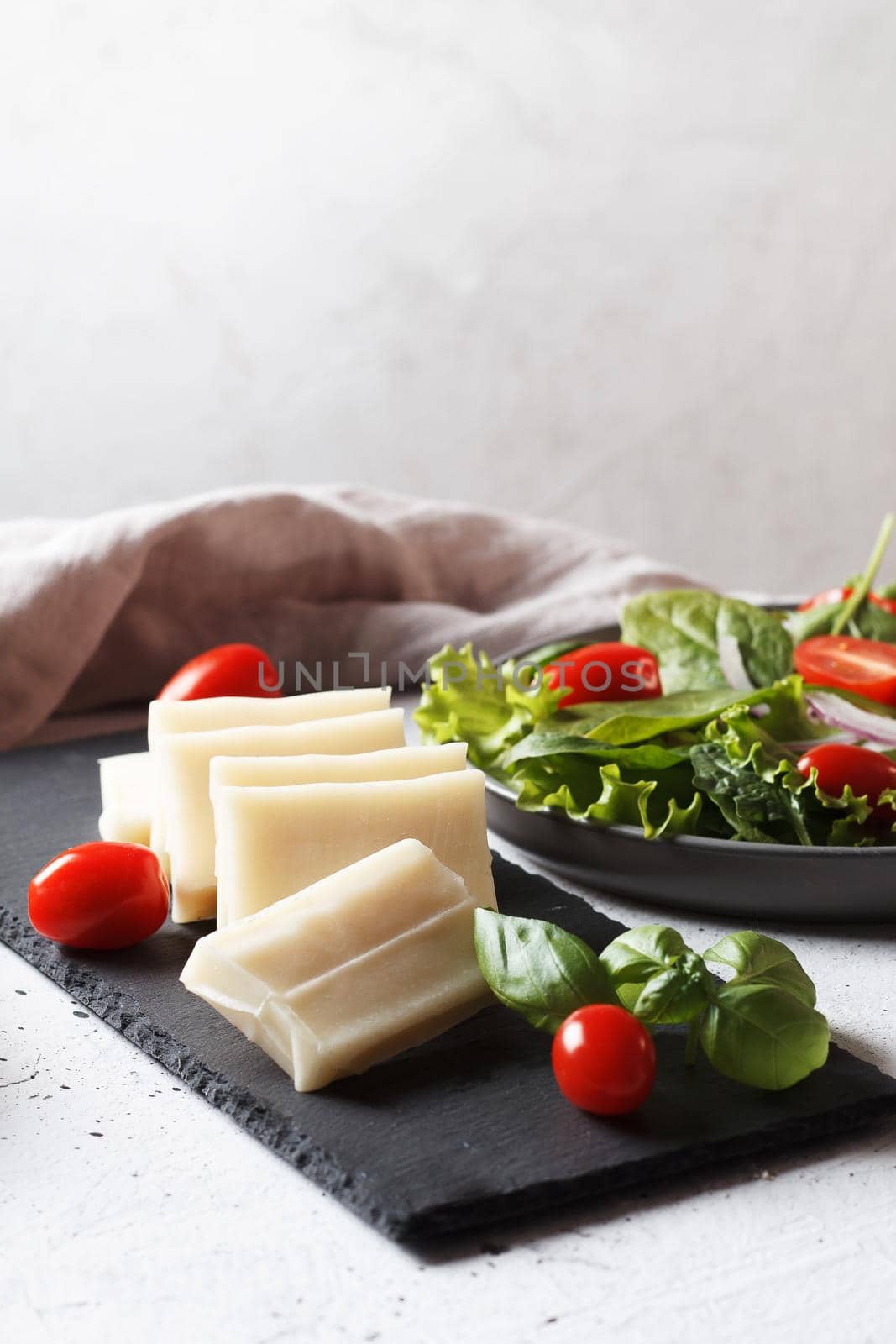 A piece of fresh sliced halloumi on a slate board with cherry tomatoes and spinach leaves. Preparing to cook cheese on the grill. Copy space. by lara29