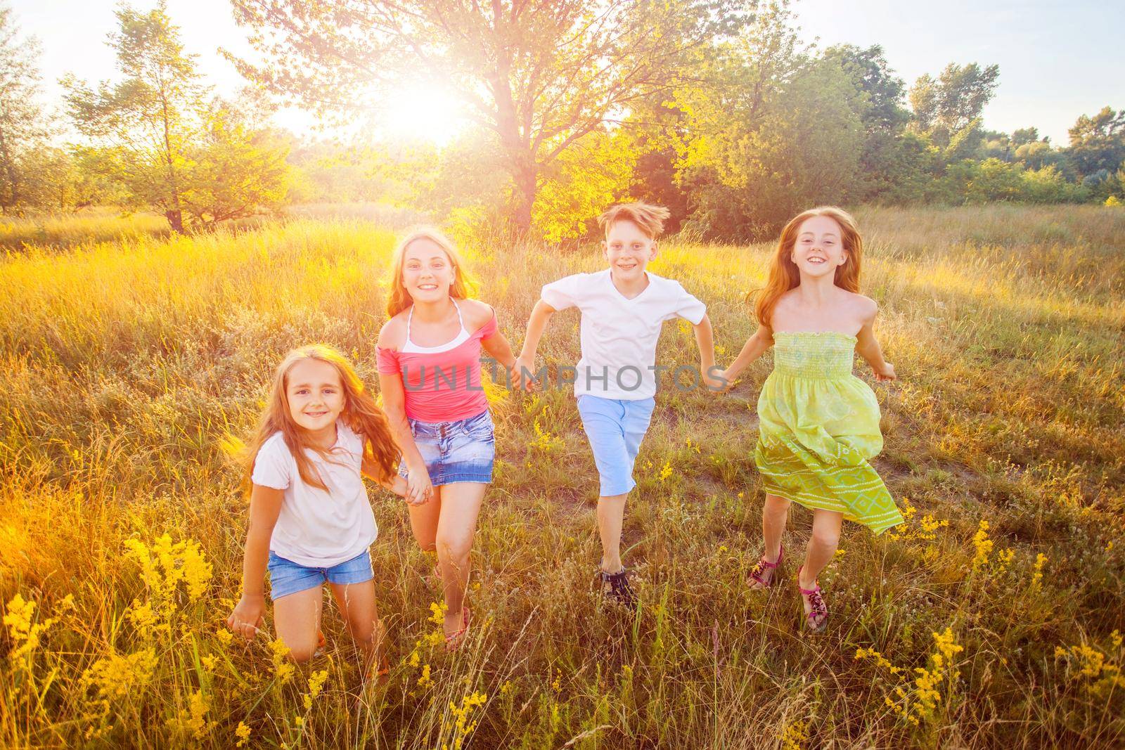 four happy beautiful children running playing moving together in the beautiful summer day. jumping and looking at camera with happiness and toothy smile.