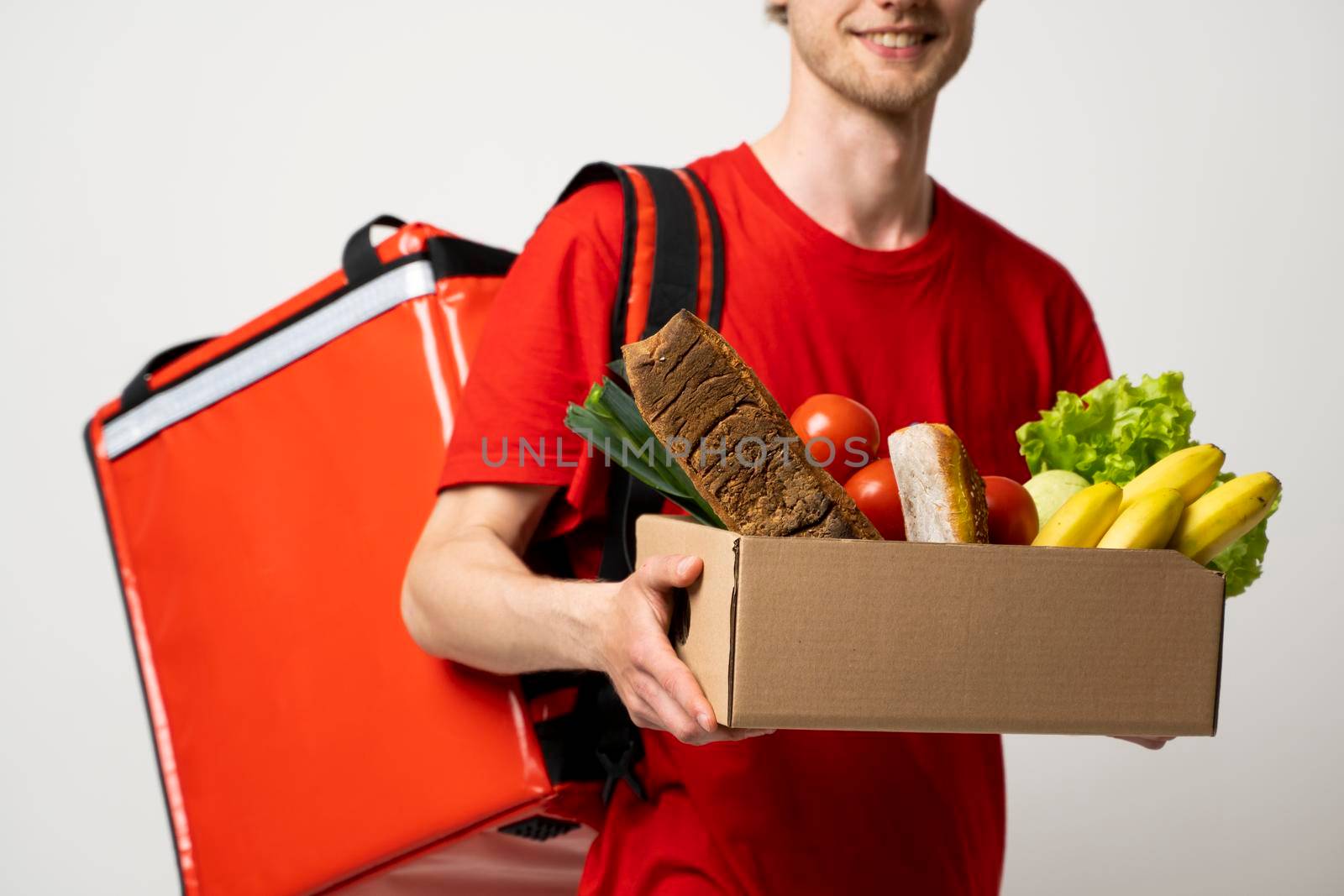 Food shipping, profession and people concept. Happy smiling delivery man with pepper box full of vegetables and thermal bag on a shoulder on white background. by vovsht