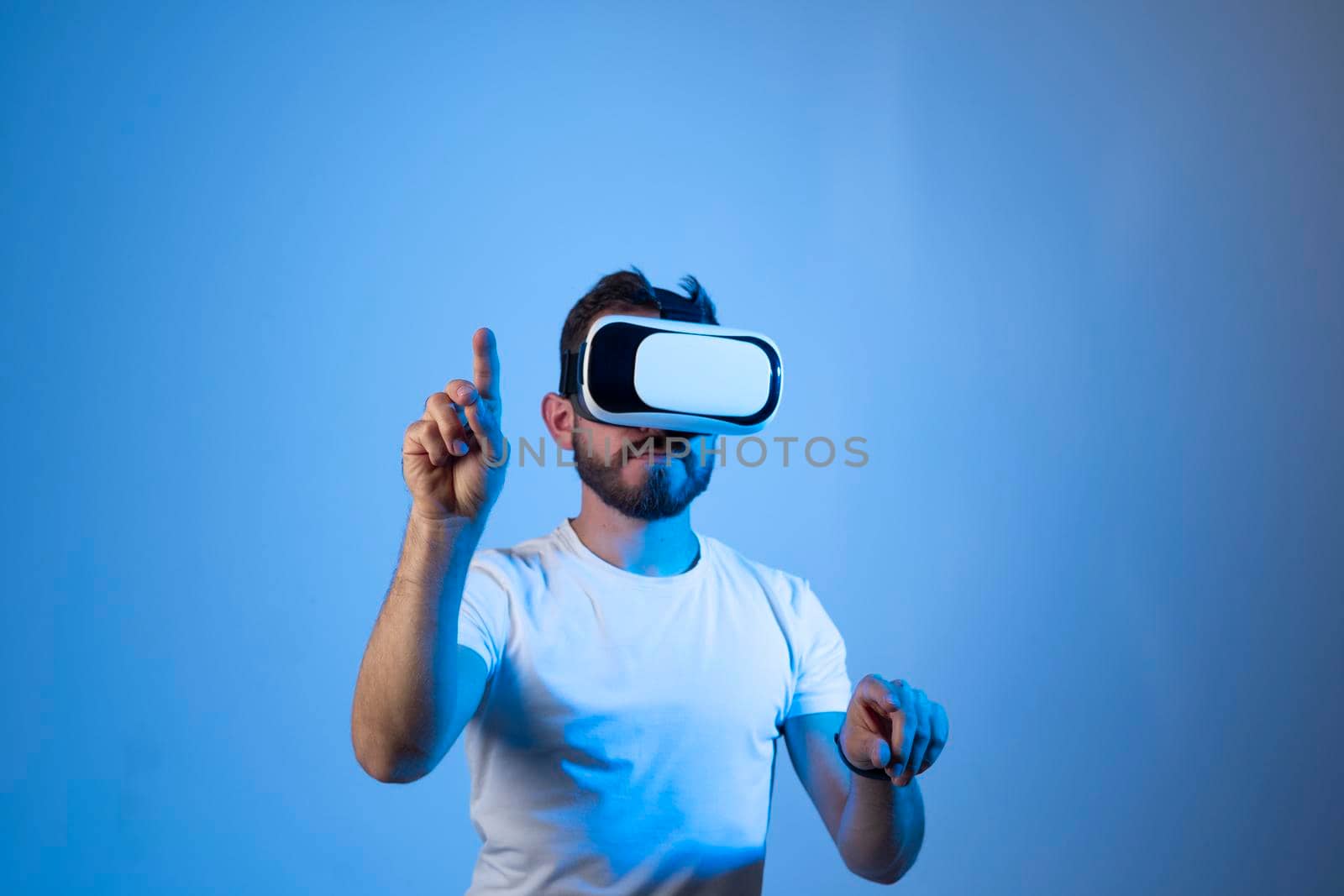 Young bearded man in virtual reality helmet plays online game in metaverse. Game simulates behavior in fictional world, gadgets and virtual reality addiction. Future technology concept