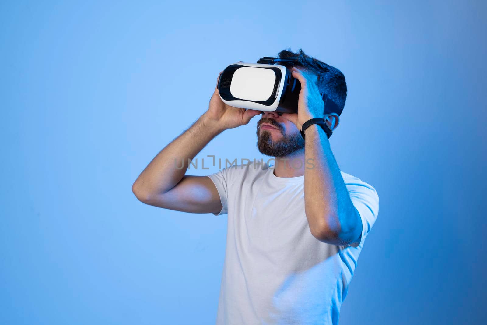 Amazed young bearded man, wearing high tech smart vr goggles, watching 360 degree video or playing a video game in metaverse. by vovsht