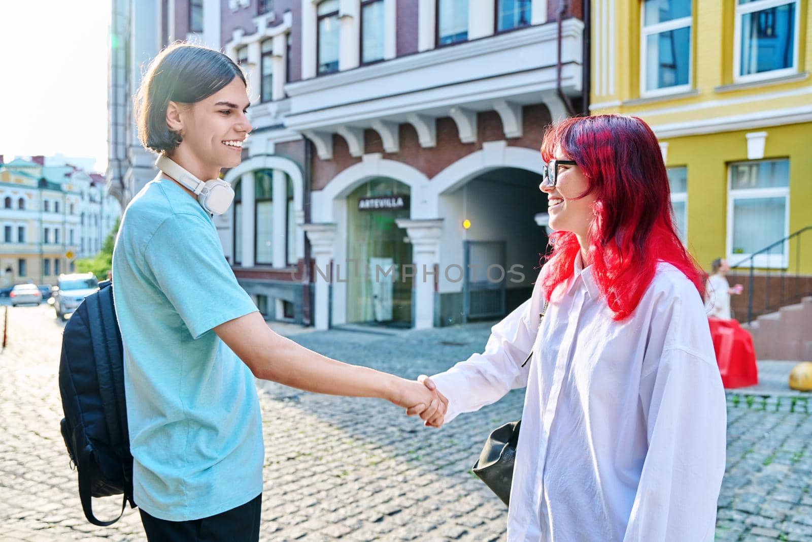 Meeting, shaking hands teenage male and female friends on the city street. Fashionable having fun teenagers guy and girl together. Friendship, communication, holidays, lifestyle, youth, urban style