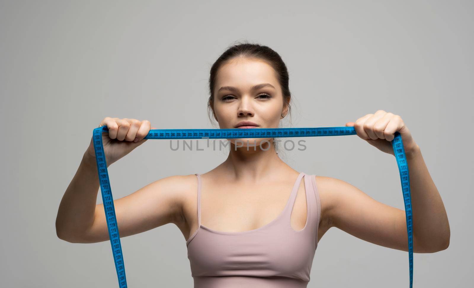 Brunette girl woman holding a centimeter tape in front of her face and look in camera on a white background. The concept of weight loss and healthy lifestyle