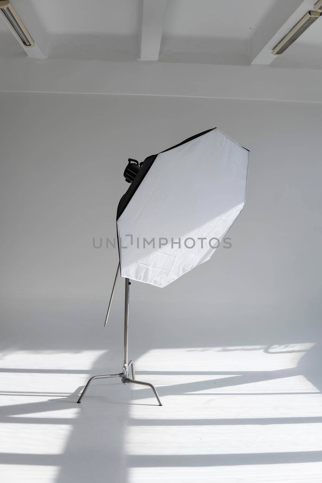 Professional photo flash light with a octbox on a c-stand on a cyclorama in modern photo studio with a huge windows. Professional lighting equipment, flashes, c-stands