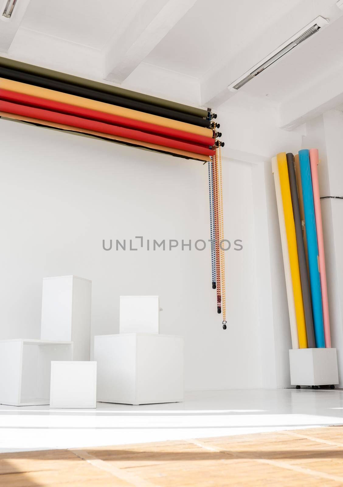 Sunny daylight photo studio interior with set rolls of color background and white cubes as a photo requisite