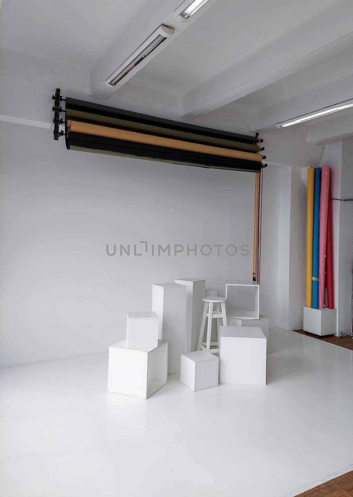 Daylight photo studio interior with set of professional equipment as a rolls of color background and white cubes on a white floor