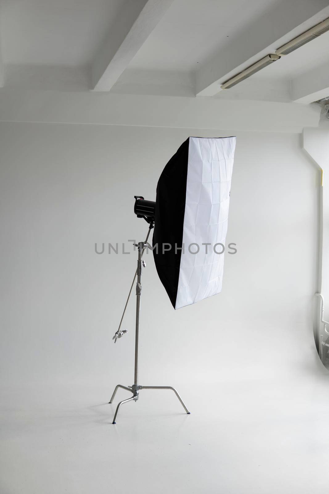 Professional photo flash light with a big softbox on a c-stand on a cyclorama in modern photo studio with a huge windows. Professional lighting equipment, flashes, c-stands