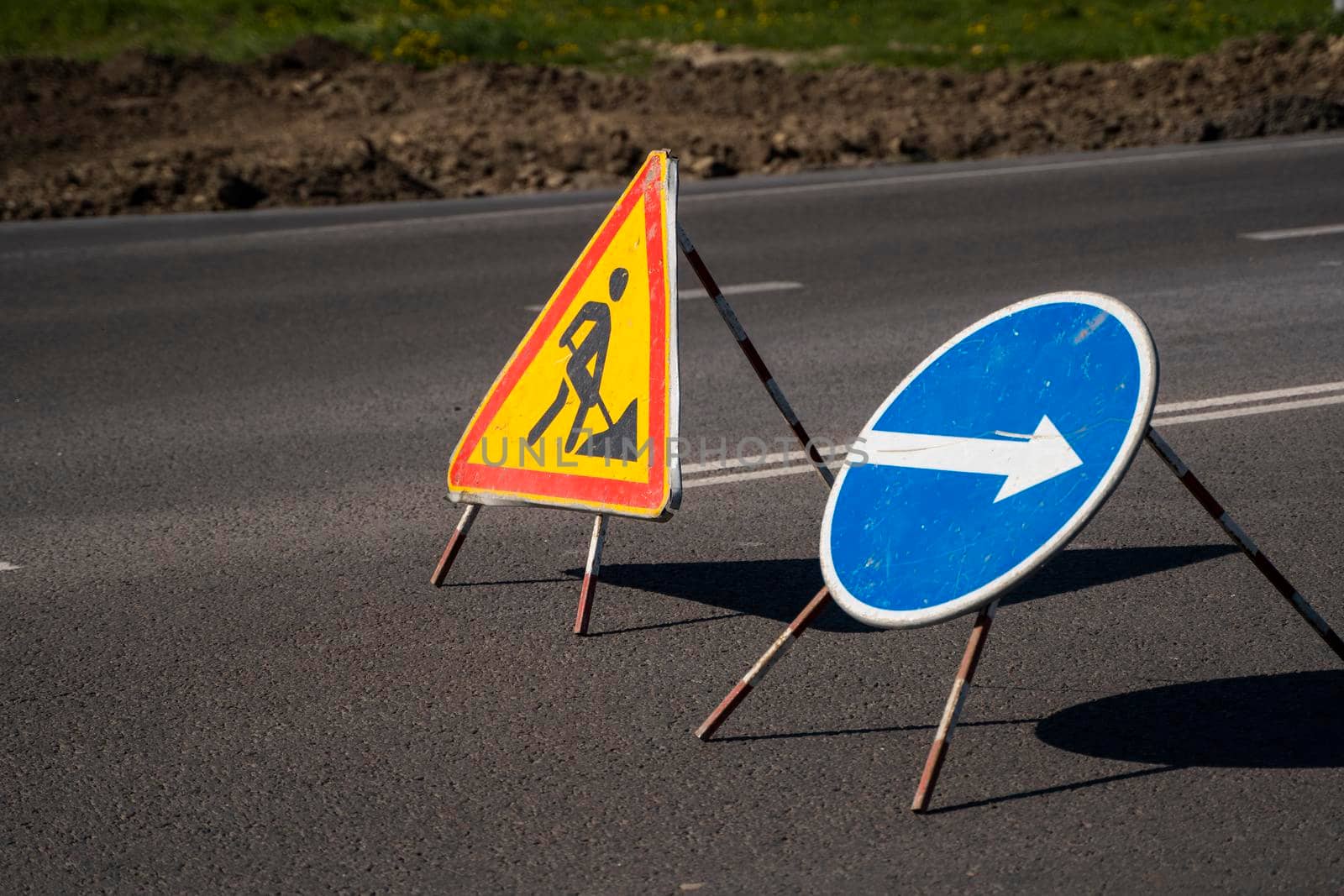 Road signs indicating the repair of asphalt and the direction to bypass the dangerous section. Repair work in the middle of the carriageway, selective focus