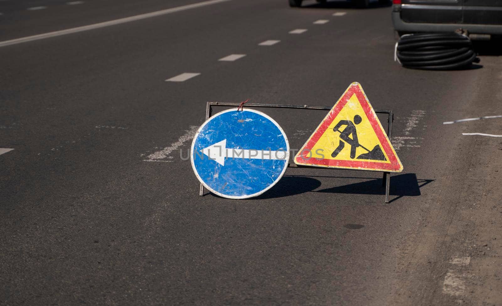 Road works sign on the road. Repair of road signs and a bypass arrow against the background of a torn road. Repair work in the middle of the carriageway, selective focus