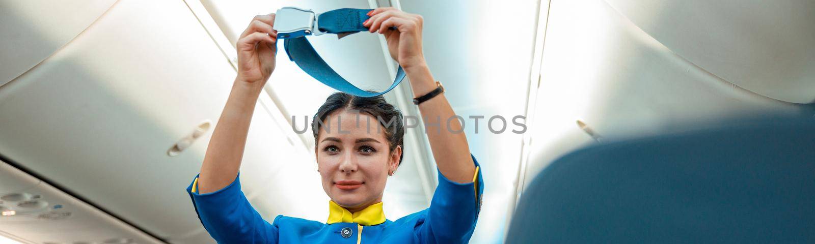 Woman stewardess demonstrating how to use safety belt in aircraft by Yaroslav_astakhov