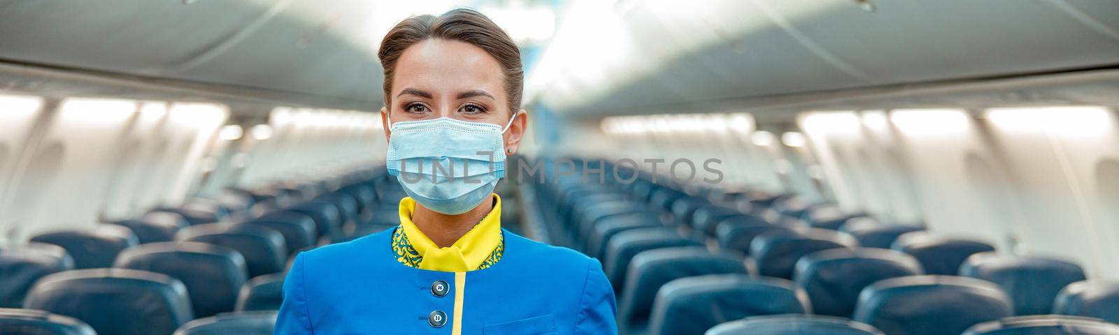 Stewardess in medical mask standing in passenger aircraft cabin by Yaroslav_astakhov