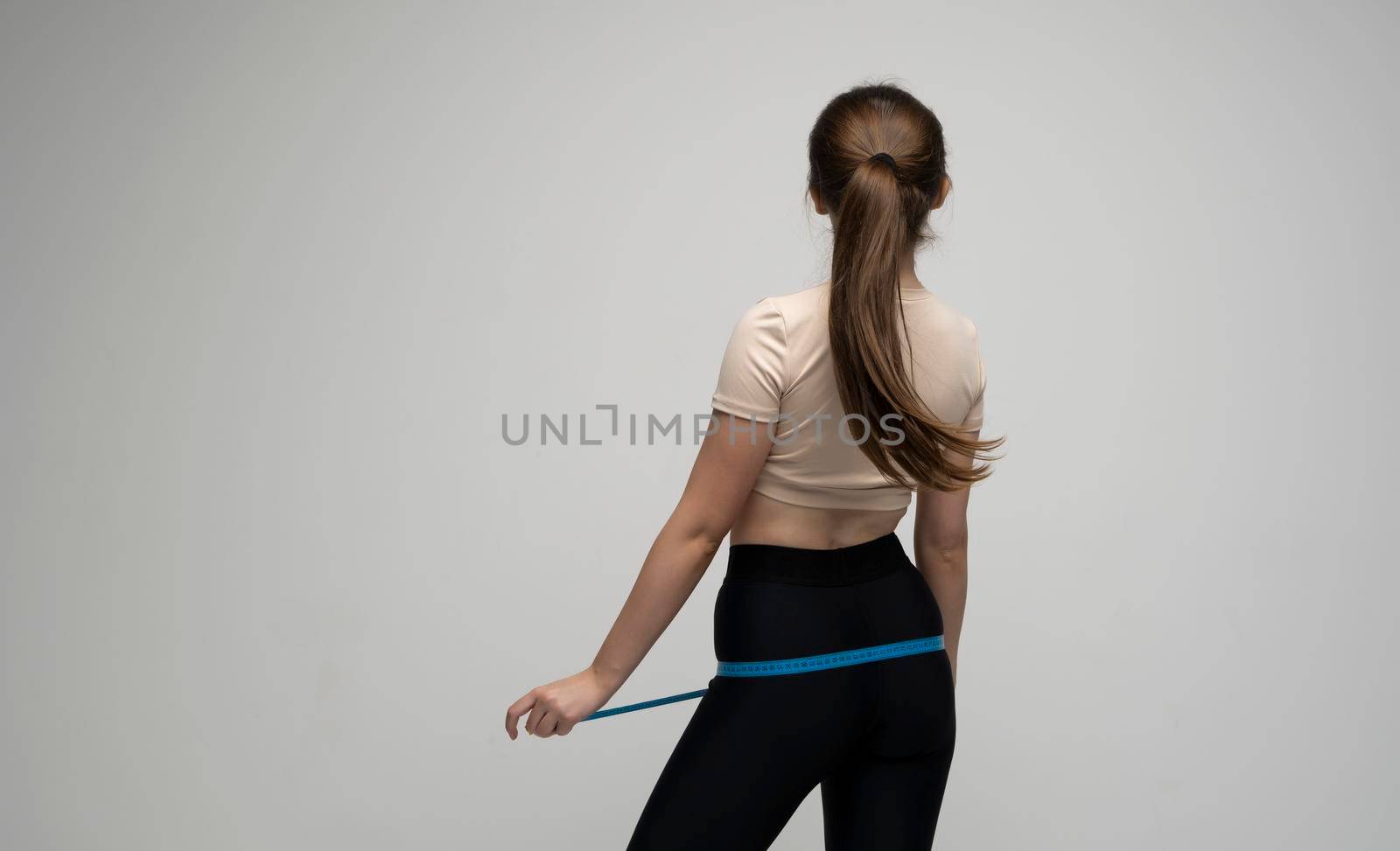 Back of slender brunette girl woman measures her hips with a centimeter on a white background. The concept of weight loss and healthy lifestyle