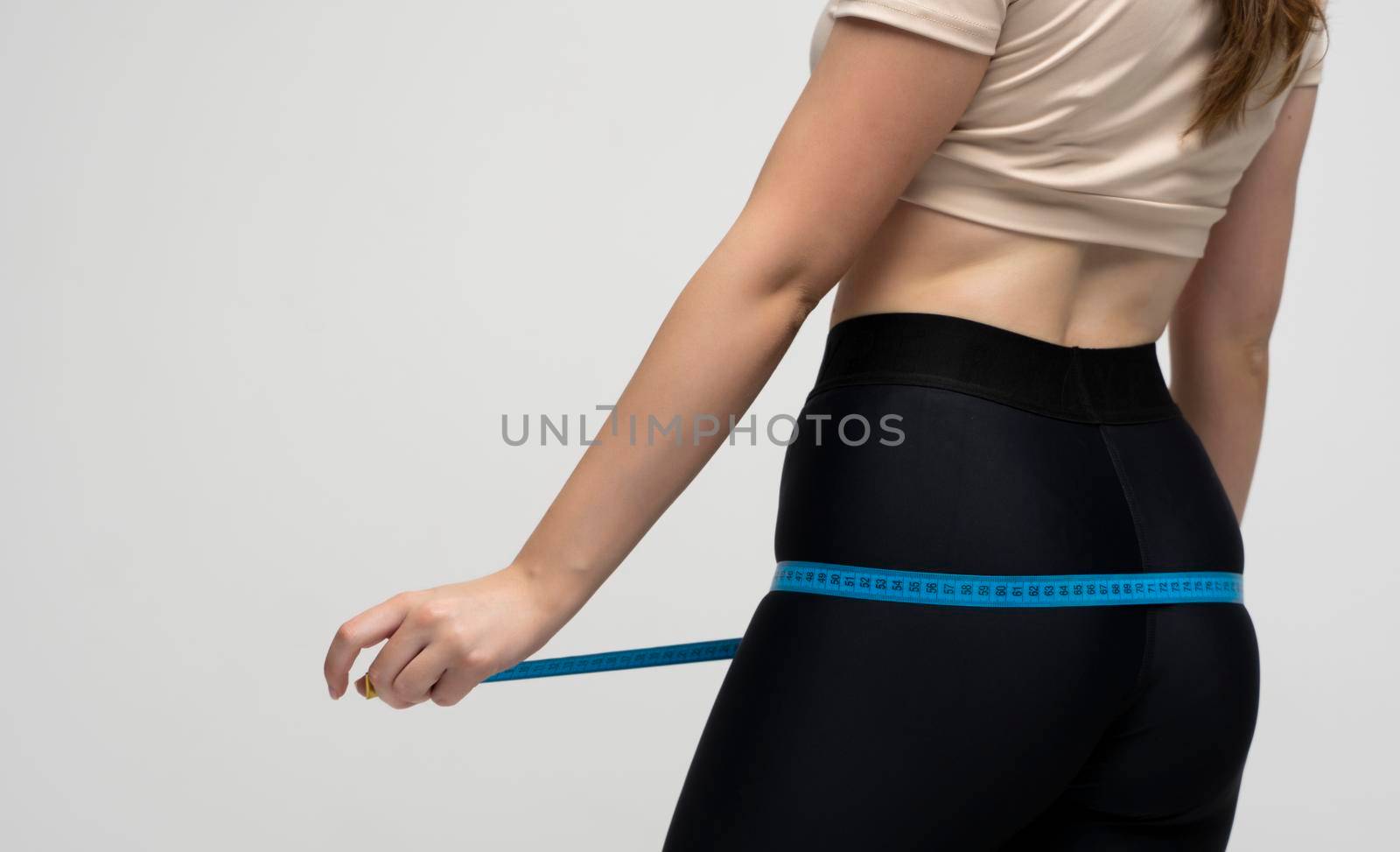 A slender girl measures her waist and hips with a centimeter on a white background. The concept of weight loss and healthy lifestyle