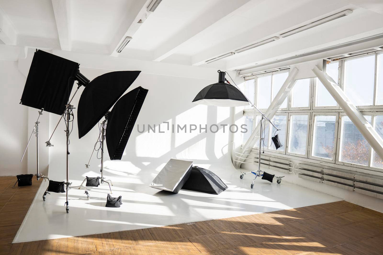 Professional lighting equipment, flashes, c-stands on a cyclorama in modern photo studio with a huge windows. Octabox, stripbox, softbox, buety plate and other stuff for photography