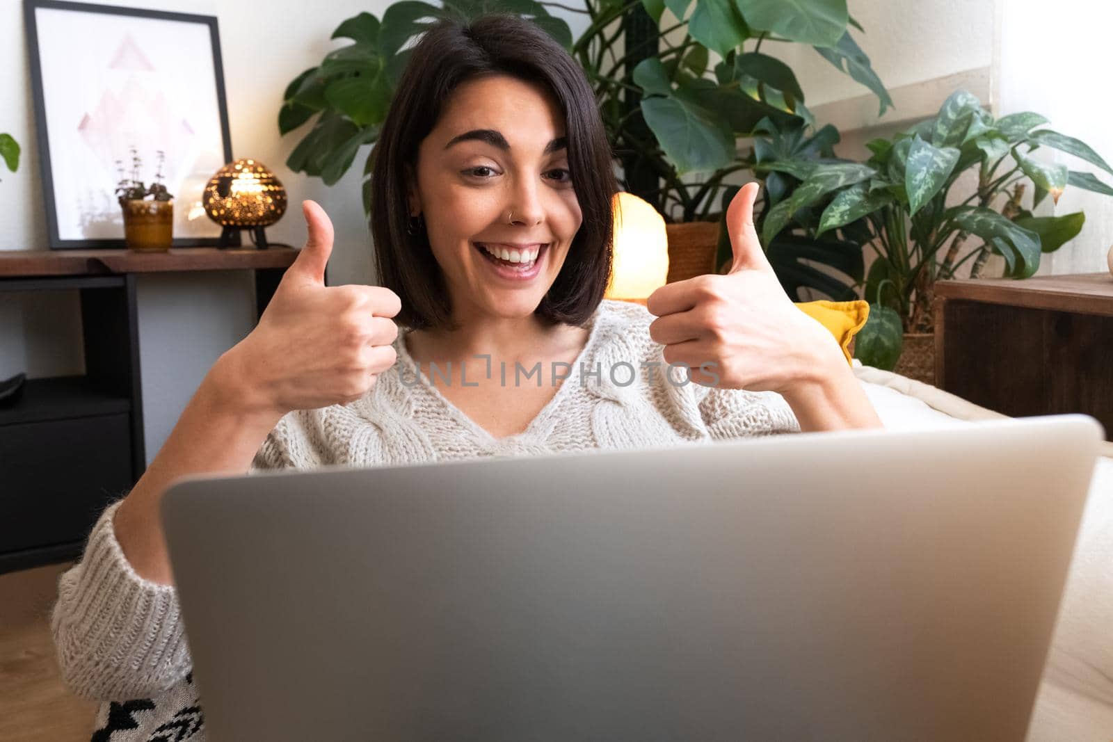 Excited young caucasian woman shows thumbs up during online video call at home. by Hoverstock