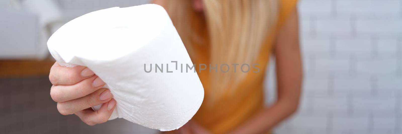 A woman is sitting on the toilet with toilet paper in her hand, close-up, blurry. Abdominal pain, diarrhea, constipation