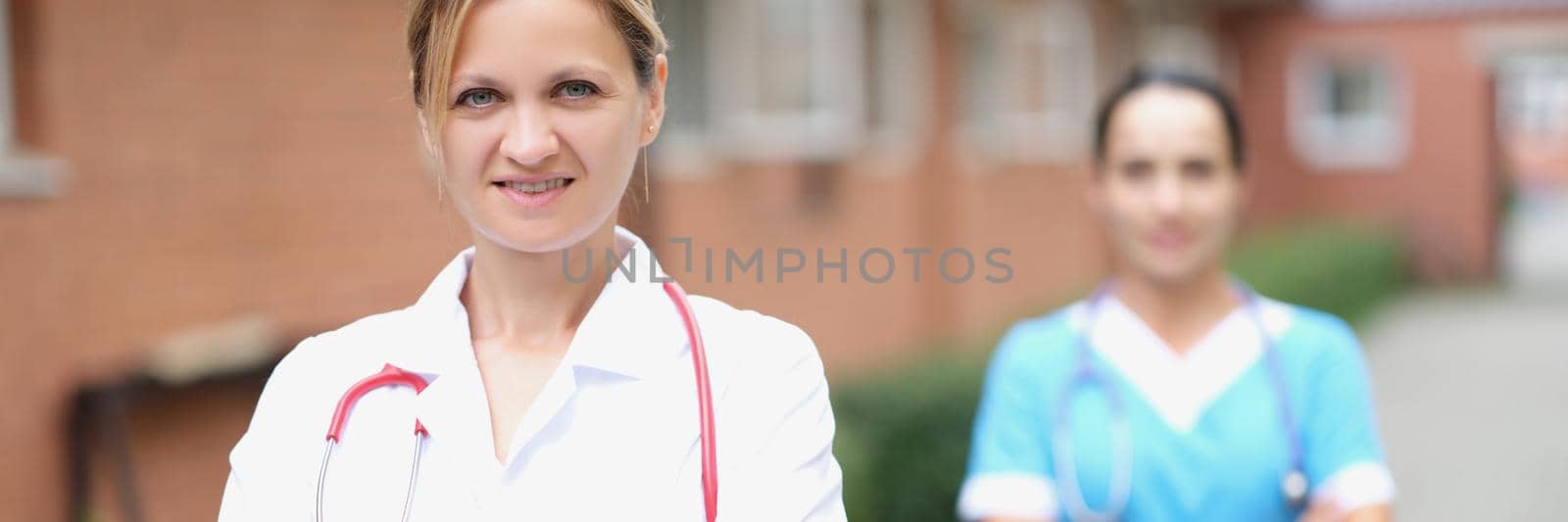 Woman doctor and nurse stand near the clinic, close-up, blurry. Rehabilitation center staff for alcoholics