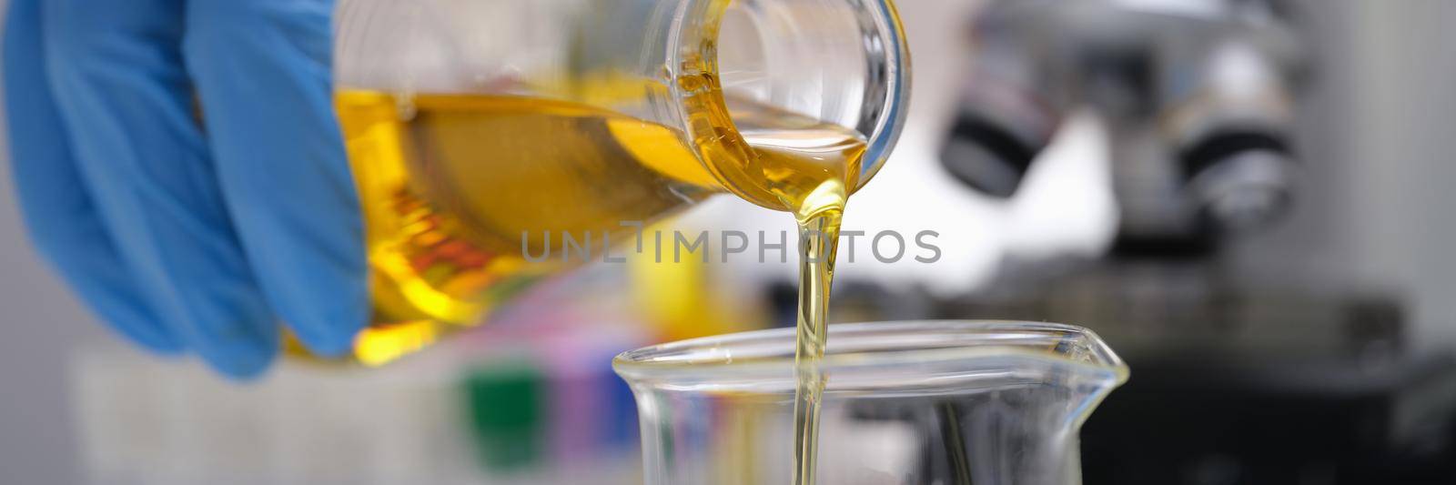 A hand in a glove pours a yellow liquid in the laboratory, close-up, blurry. Optical microscope, urine analysis