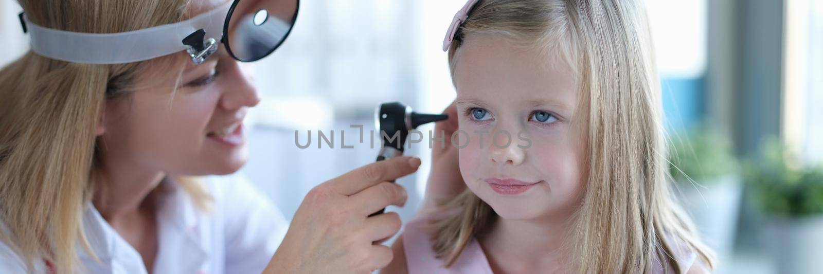 A woman otolaryngologist in a clinic looks at the ear of a little girl. Children's doctor, diagnosis of diseases, consultation