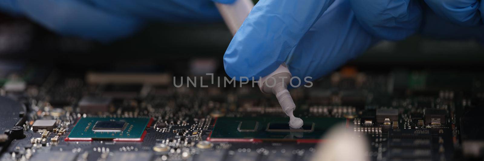 Gloved hands hold thermal paste on a laptop chip, close-up. Cleaning laptop from dust, service center