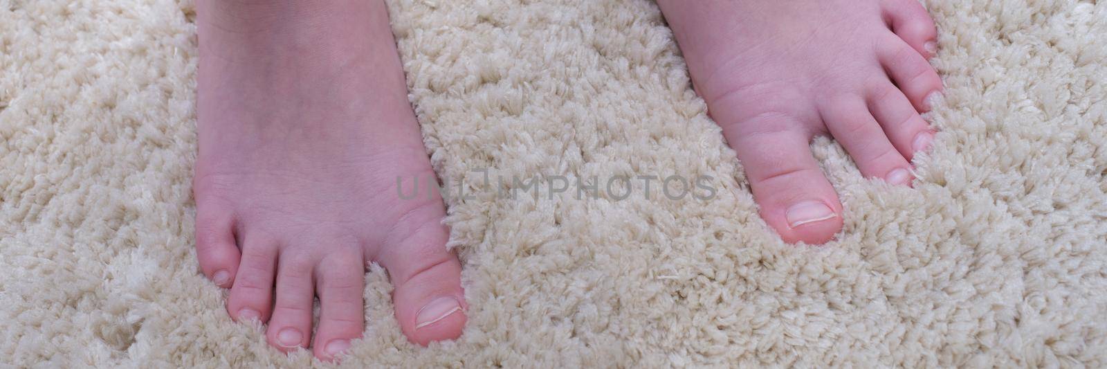 Bare feet of a man on a warm beige carpet, close-up. Soft pile carpet for an apartment. Noise isolation, foot massage