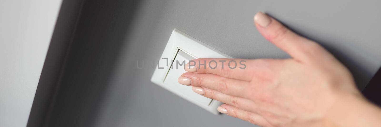 A woman's hand presses a white switch on a gray wall, close-up. Devices for switching off electric lighting
