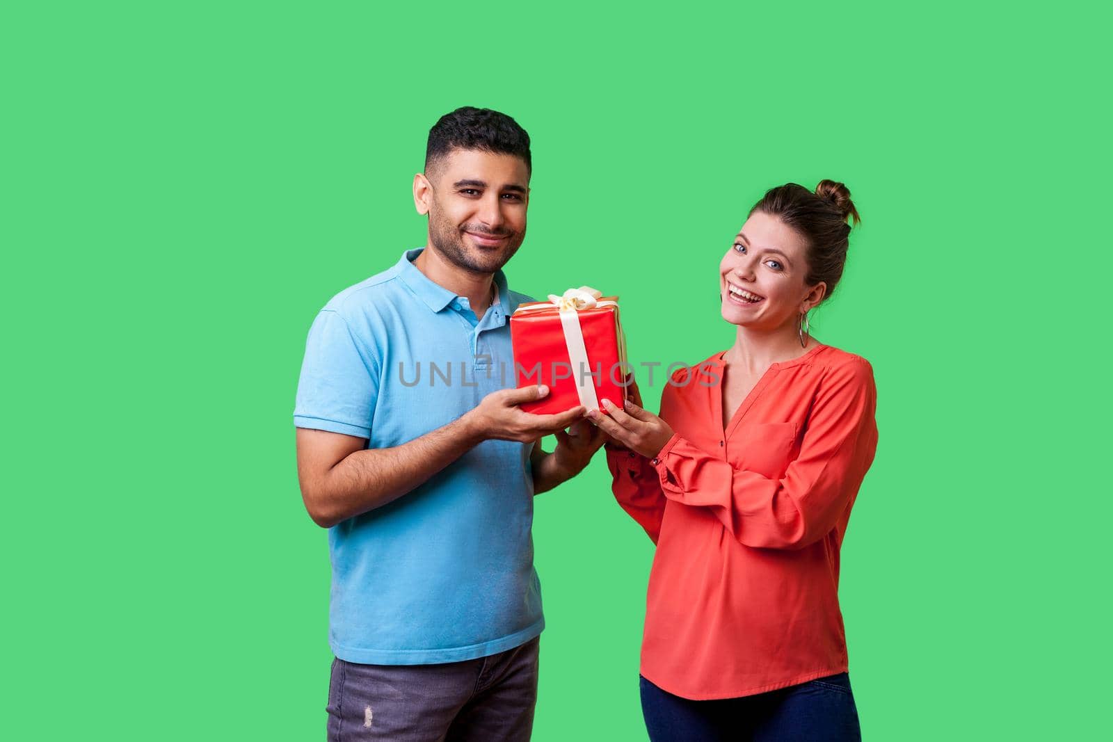 Gift for family. Portrait of happy couple in casual wear standing, holding box with present and looking at camera together, enjoying holiday surprise. isolated on green background, indoor studio shot