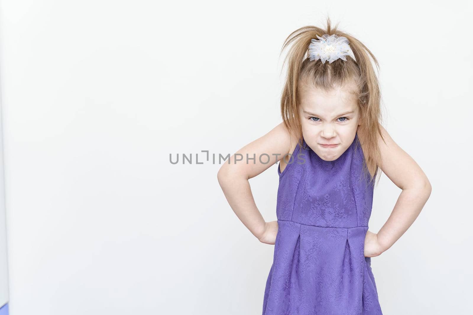 cute upset little girl in a blue dress. hands at sides, anger emotion. gray background with place for text