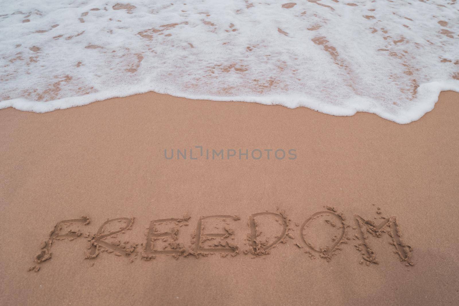 Freedom word hand drawn on sand summer beach background.