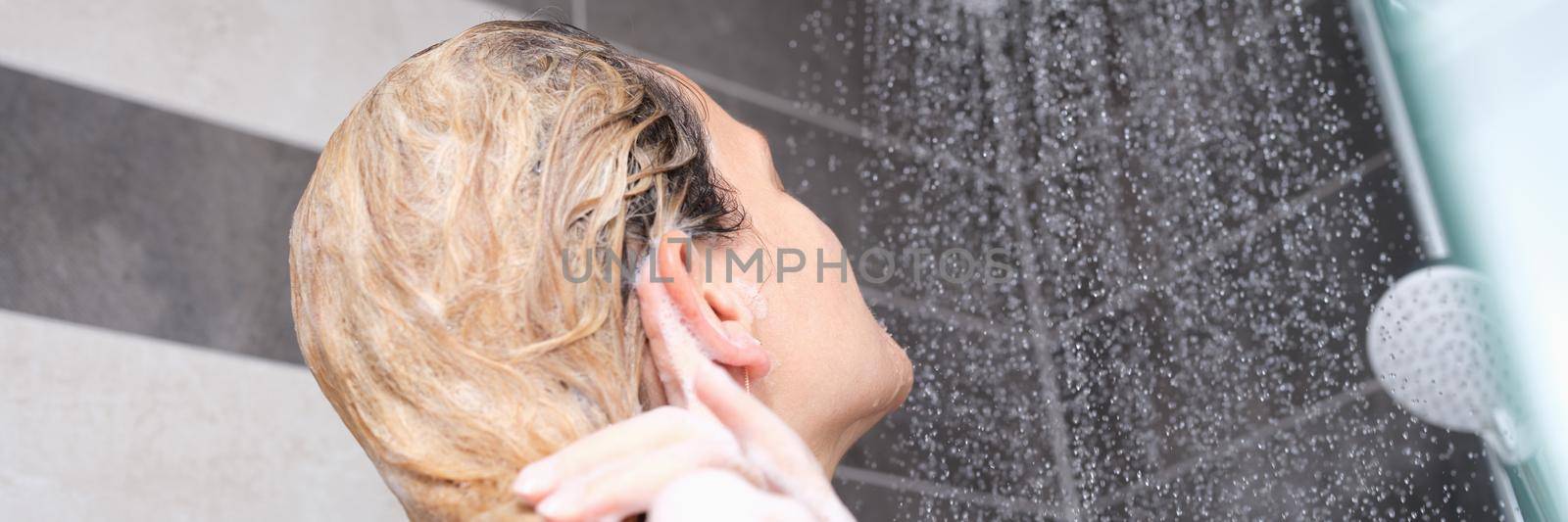 A woman washes her hair with shampoo in the shower by kuprevich