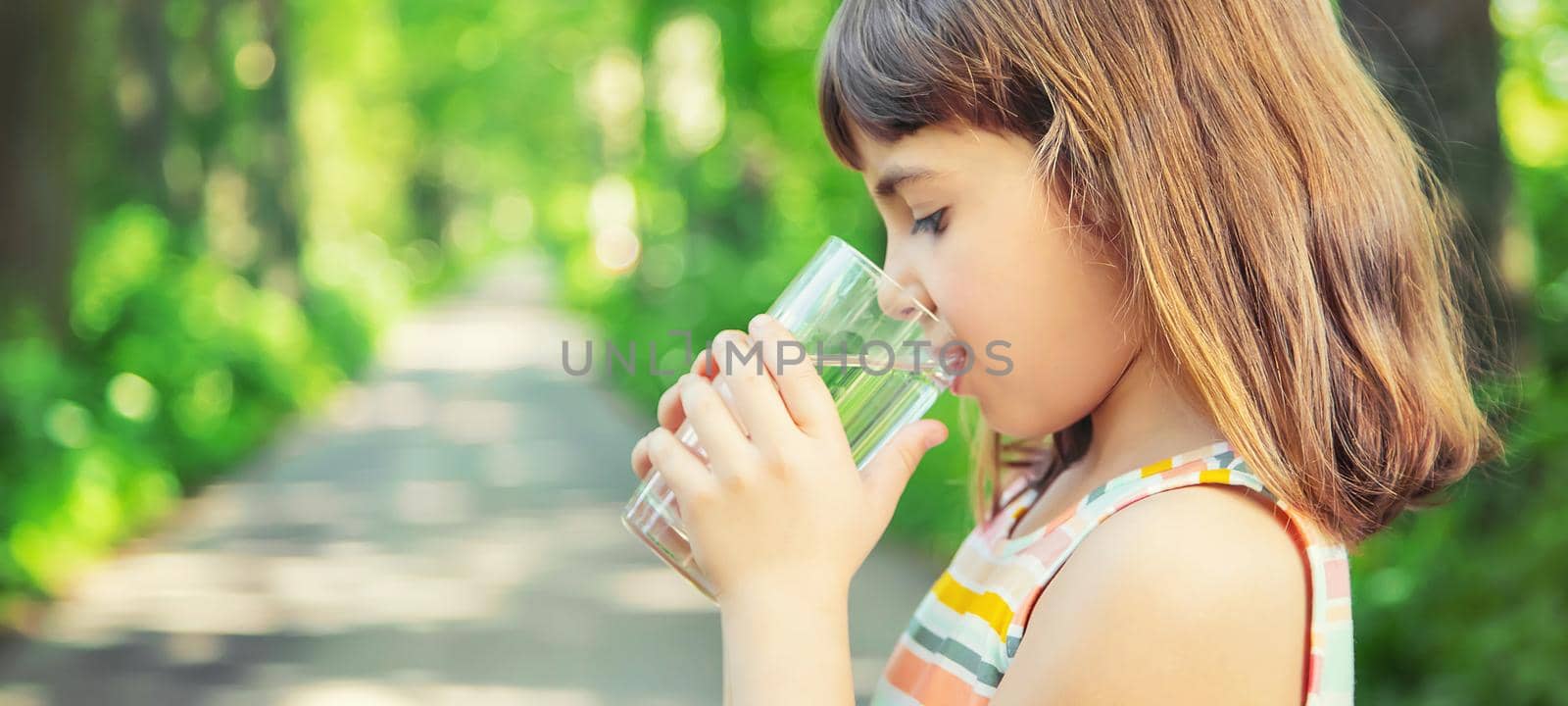 A child drinks water from a glass on the nature. Selective focus. Drink.