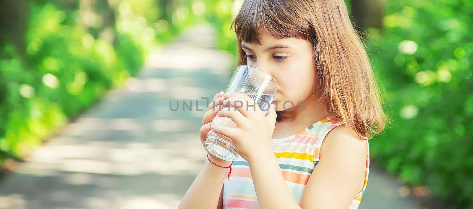 A child drinks water from a glass on the nature. Selective focus. by yanadjana
