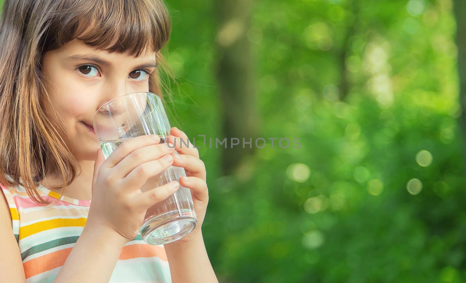 A child drinks water from a glass on the nature. Selective focus. Drink.