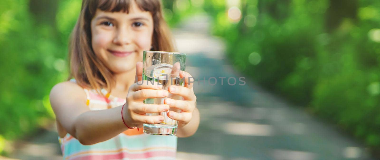 A child drinks water from a glass on the nature. Selective focus. by yanadjana