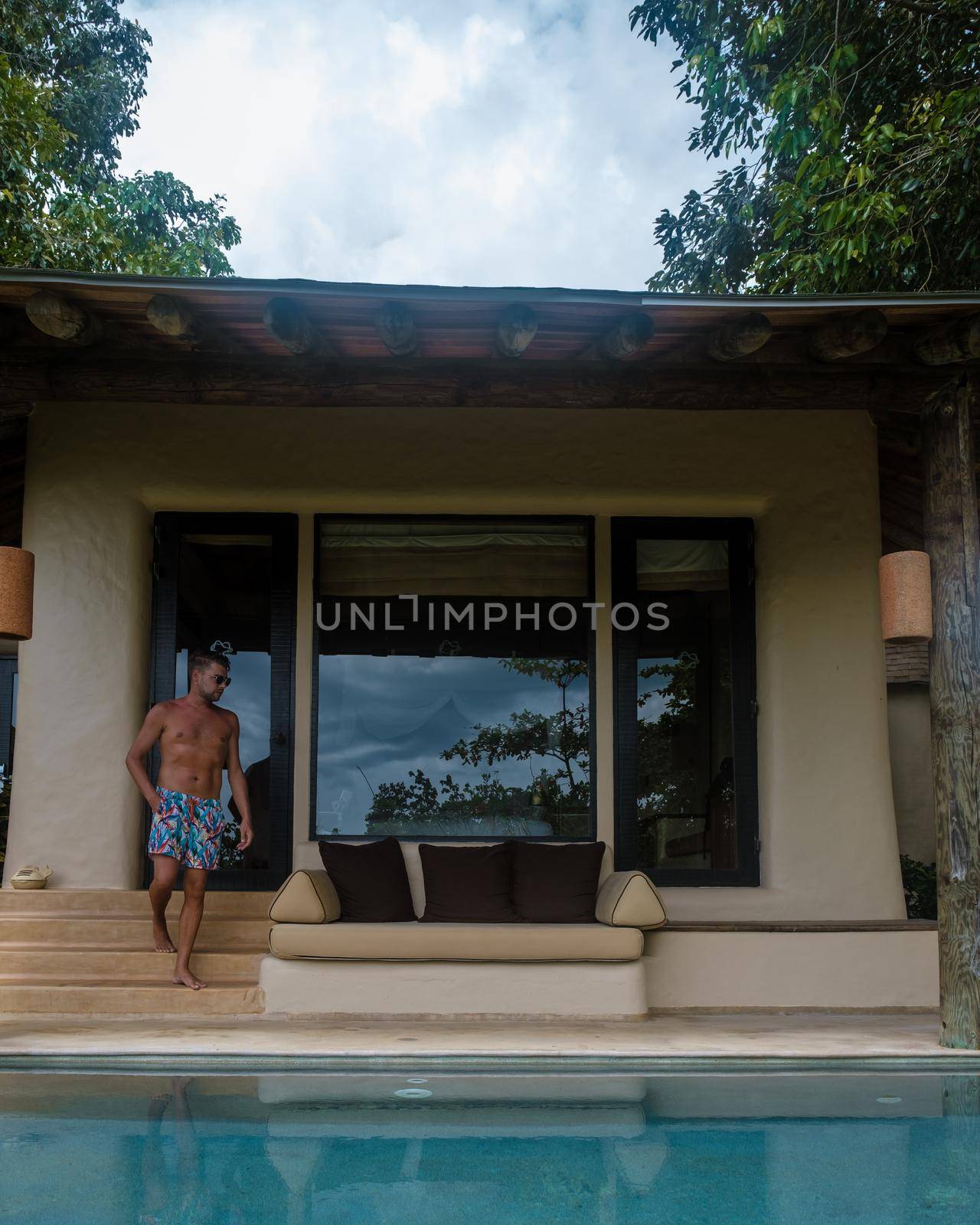 European man at infinity pool looking out over the ocean, luxury vacation private pool villa, luxury retreat