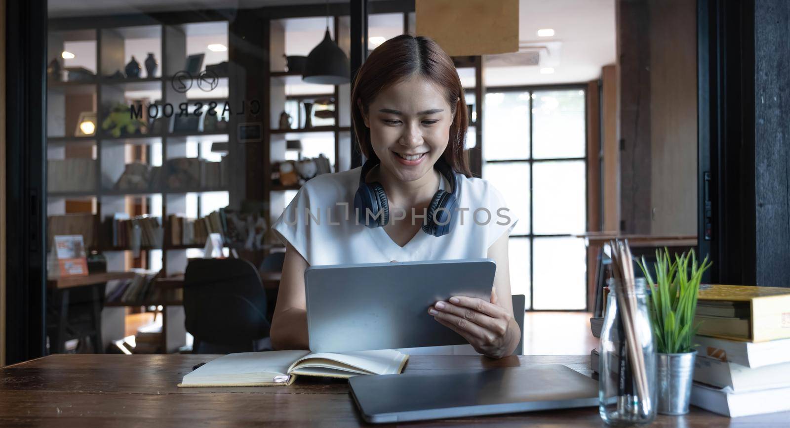 Smiling Asian young female using headset looking at laptop screen listen and learning online courses. Happy chinese business woman with headphones video call for customer service by wichayada