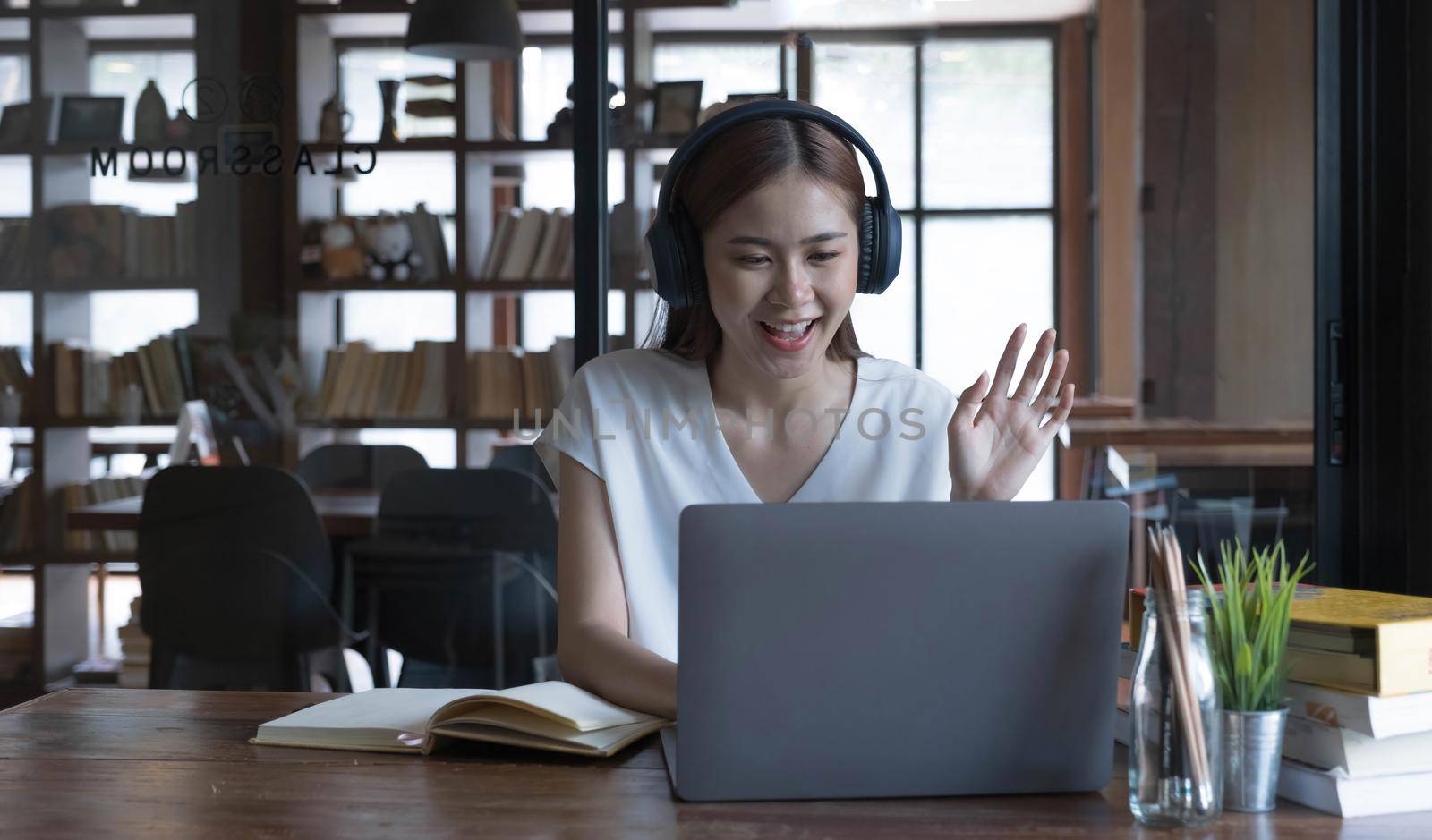 Smiling asian undergraduate teen girl student study in library with laptop books doing online research for coursework, making notes for essay homework assignment, online education e-learning concept by wichayada